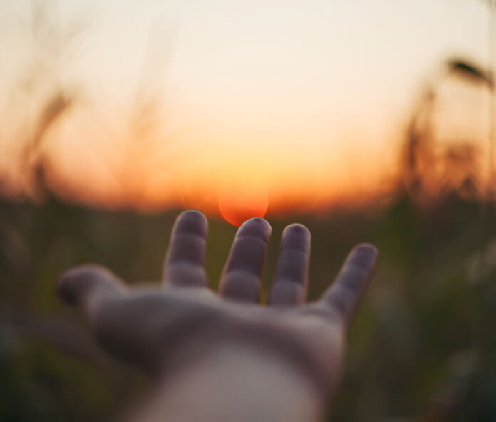 Braço estendido com mão estendida suavemente para o nascer do sol.